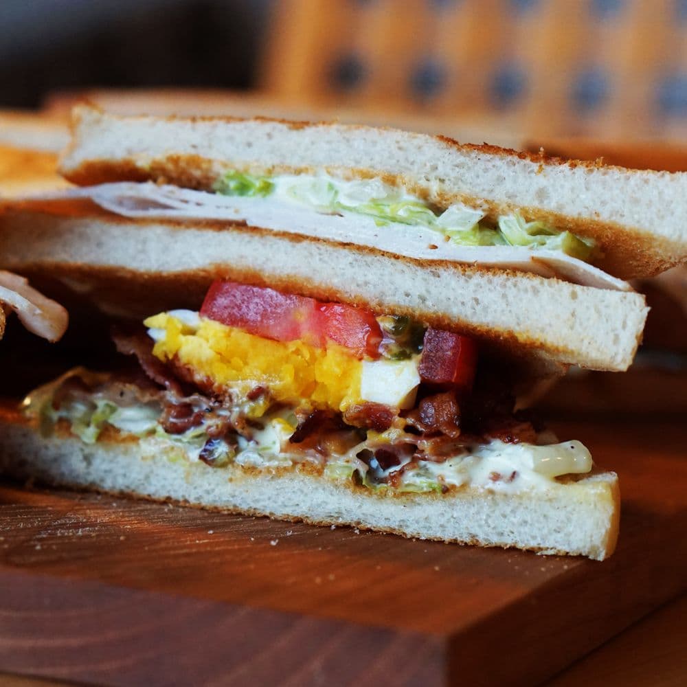 A stacked club sandwich with turkey, bacon, tomato and lettuce on toasted sourdough